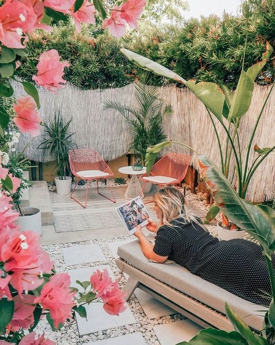 a gorgeous tropical patio with pink chairs and pink blooms, a comfy daybed, potted tropical plants