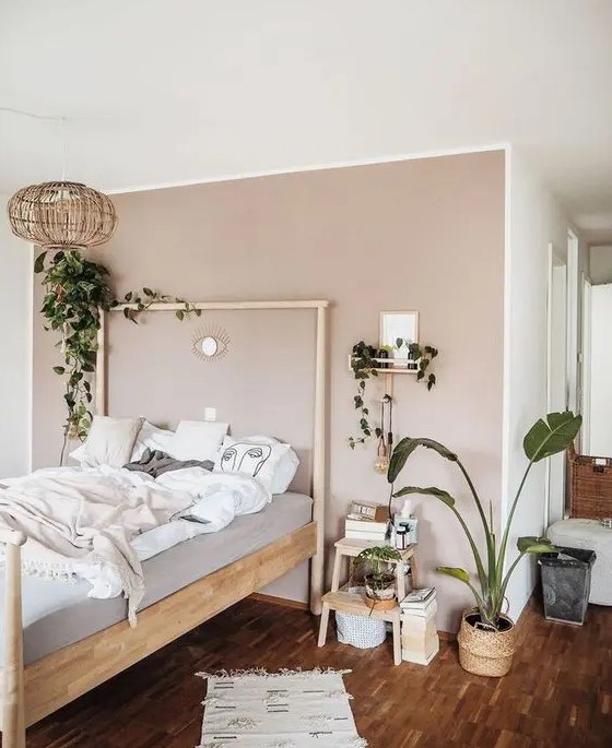 a lovely Scandi bedroom with a blush accent wall, a wooden bed and a stool, potted plants and a woven pendant lamp