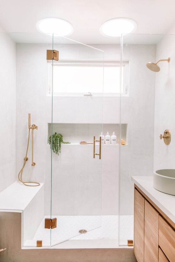 a lovely neutral bathroom with white walls, a stained vanity, a bench and a niche in the shower, gold fixtures