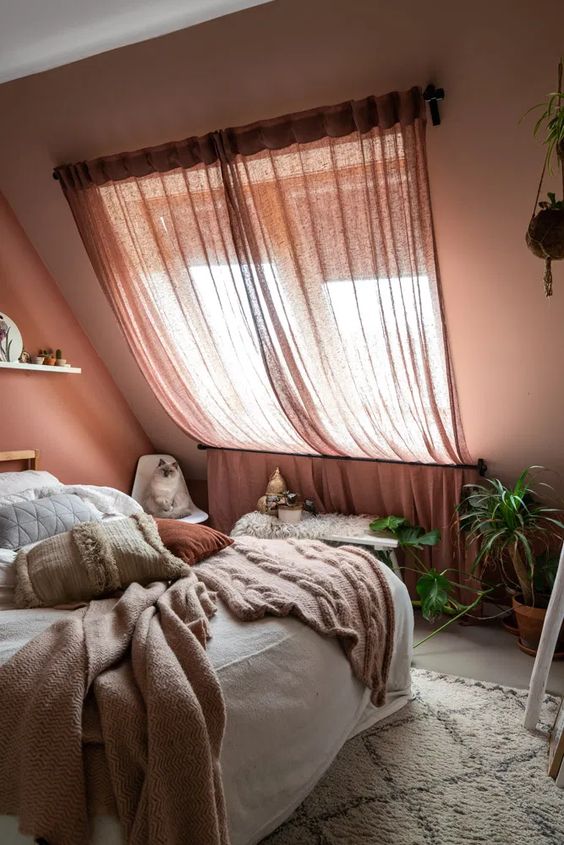 a mauve attic bedroom with a skylight, a bed with neutral bedding, potted plants and a ledge with potted plants