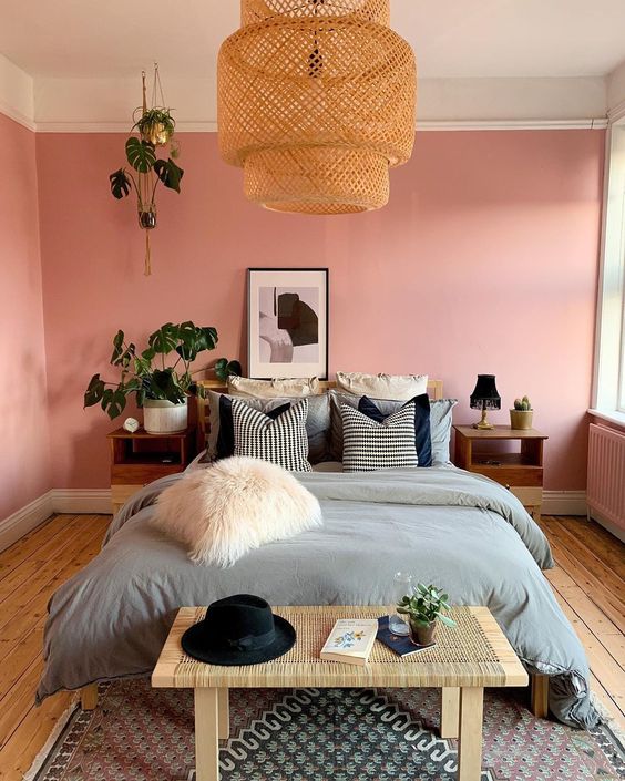 a modern meets boho bedroom with pink walls, wooden furniture, a wicker lamp, potted greenery and a faur fur pillow