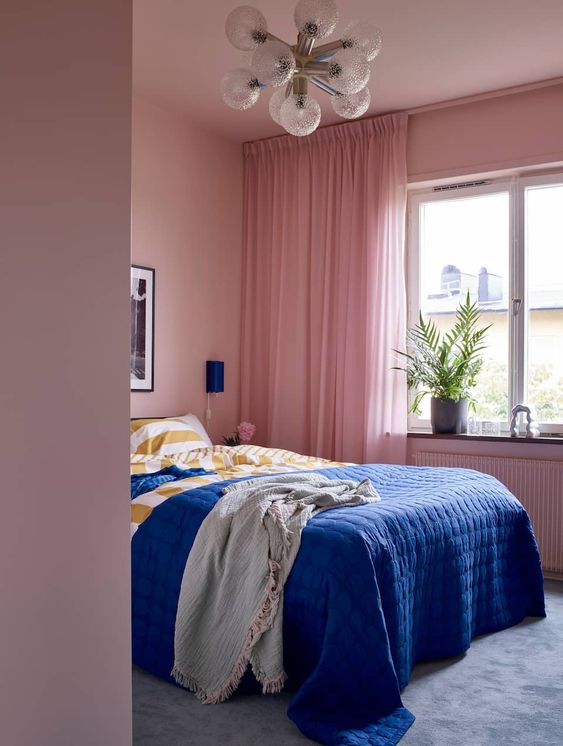 a modern pink bedroom with a bed and super bright bedding, some artwork and potted plants is a lovely and bright space