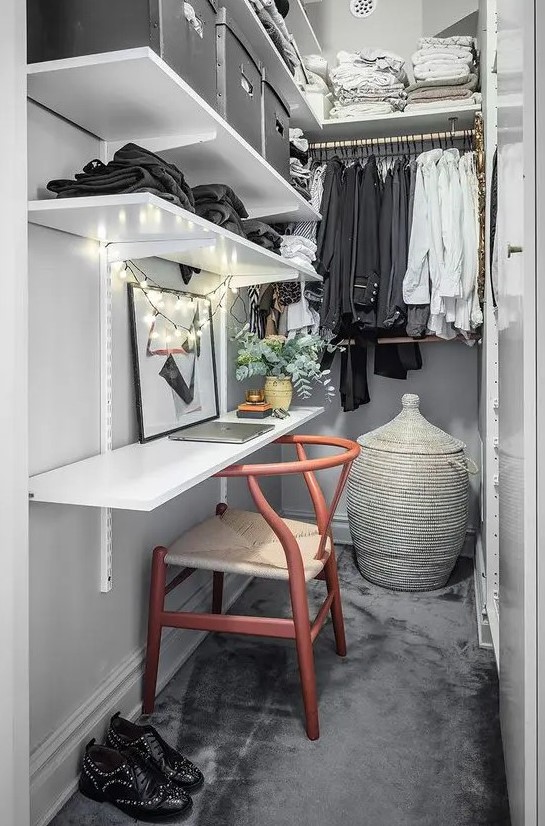 a narrow closet done with open shelves, railings, a shelf that is a desk, a chair, a basket with a lid and some lights