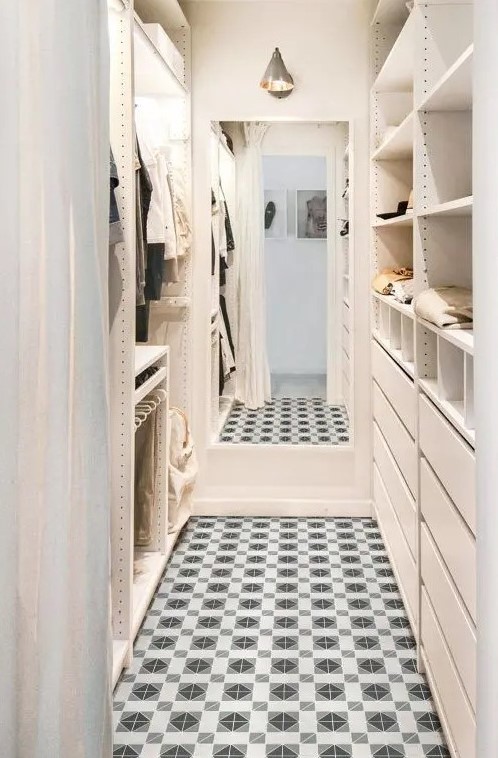 a neutral and warm-colored narrow closet with open storage compartments, drawers and shelves plus some railings and a large mirror