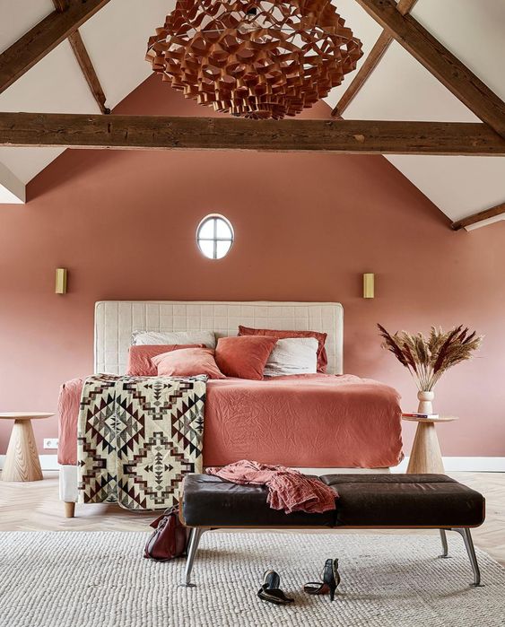 a pink attic bedroom with a white upholstered bed and rose bedding, a black leather bench, a chandelier and gold sconces