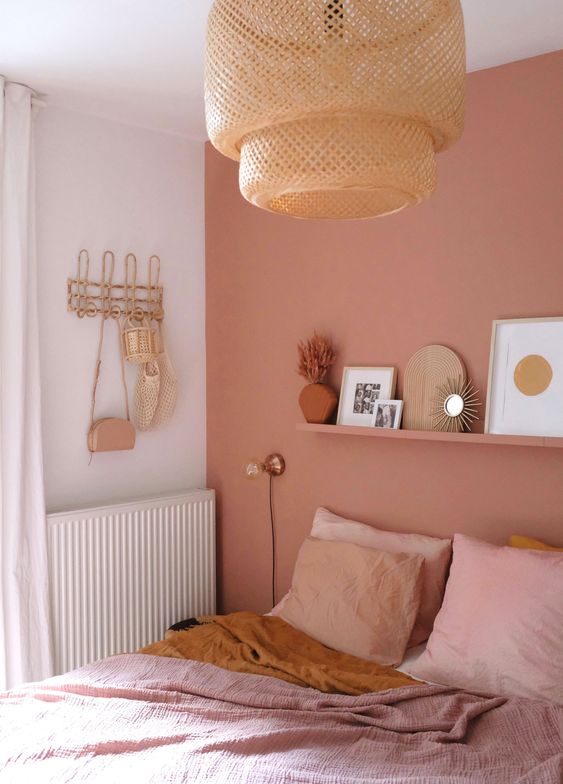 a pink boho bedroom with a ledge gallery wall, a bed with pink bedding, a woven pendant lamp and blush curtains