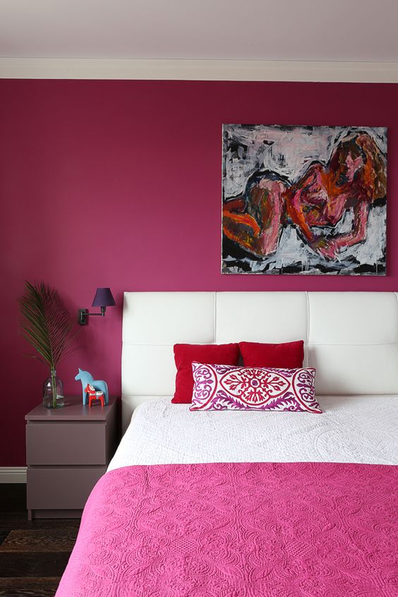 a quirky bedroom with a fuchsia statement wall and bedspread, a statement artwork, a lavender nightstand and purple sconces