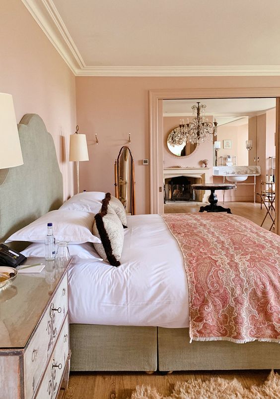 a refined blush bedroom with a grey bed and pink and white bedding, mirror nightstands, table lamps and a fluffy rug