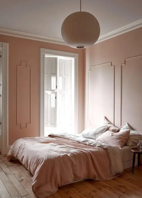 a refined vintage inspired bedorom with blush molding walls, blush and white bedding, a wooden floor and a paper lamp