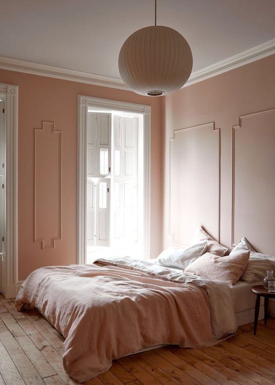 a refined vintage-inspired bedorom with blush molding walls, blush and white bedding, a wooden floor and a paper lamp