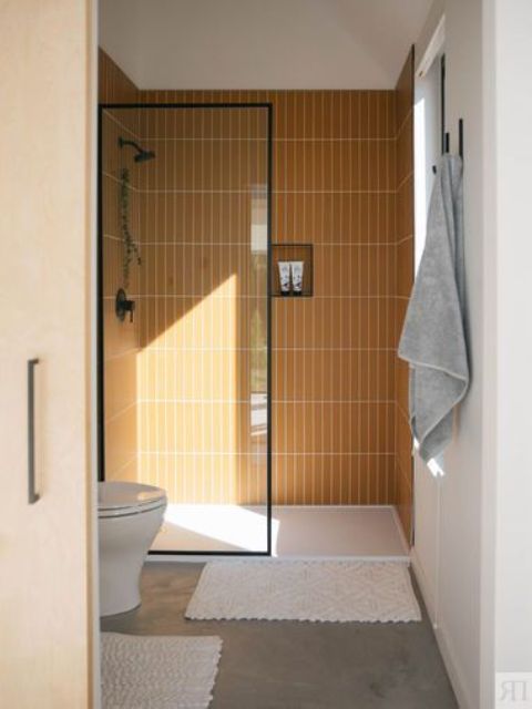 a small and bright bathroom with a shower space clad with yellow skinny tiles, a concrete floor and white appliances welcomes in