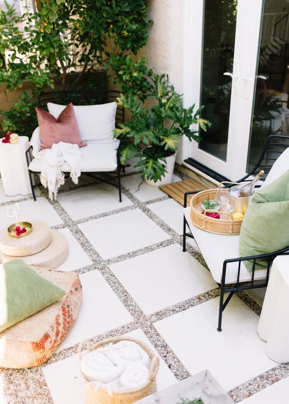 a small and bright patio with black chairs with pillows, colorful cushions on the ground, some side tables and poufs