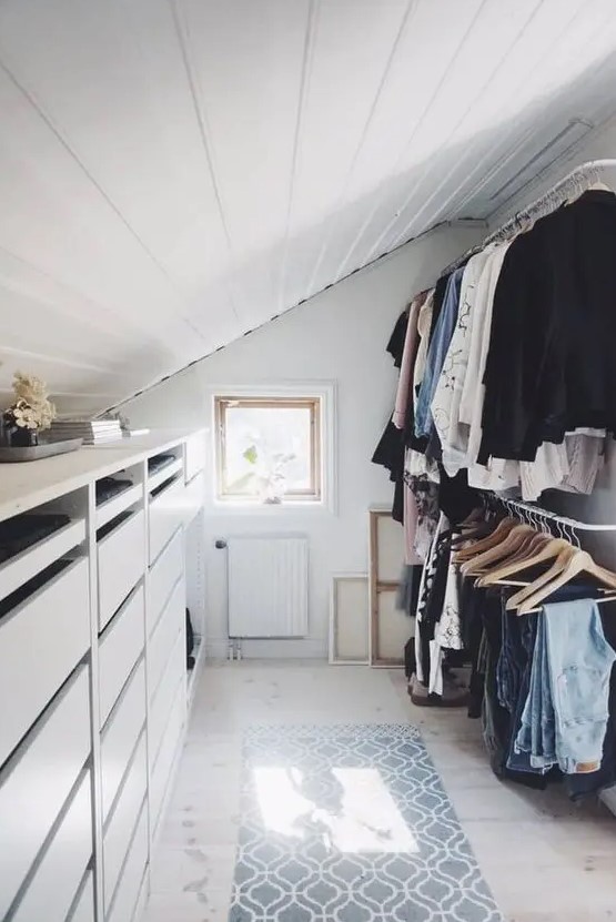 a small and cool attic closet with a dresser, railings for clothes, a printed rug and some art is a smartly organized space