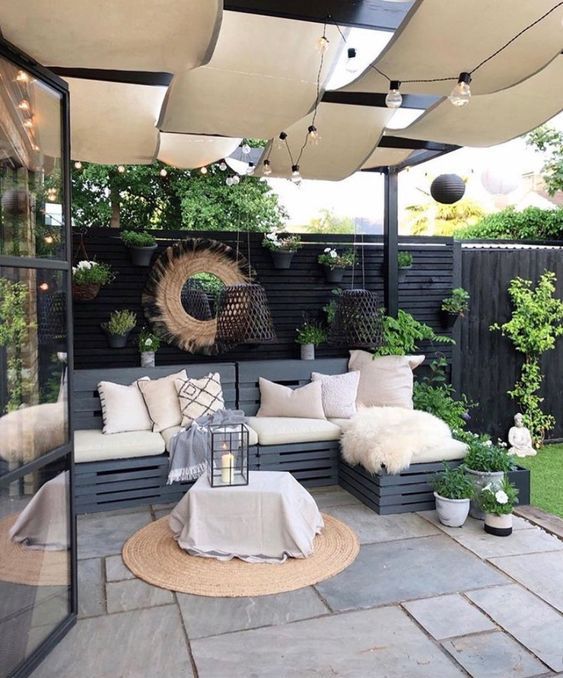 a small and cool patio with a stone deck, a wooden pallet sofa, a table, potted greenery and woven pendant lamps