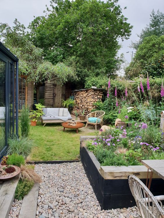 a small and cozy garden with a flower bed, some bright blooms in pots and not only, a lawn and some garden furniture