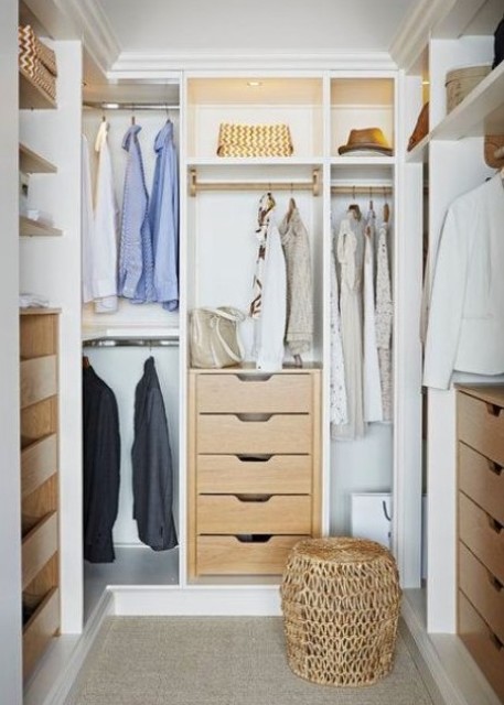 a small and cute closet with built-in shelves, drawers, built-in lights and a woven pouf plus racks for clothes