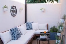 a small and cute patio with a corner sofa, side tables, potted greenery, side tables and some lights over the space