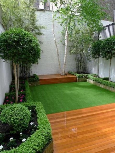 a small and elegant garden with a green lawn, with some flower beds with blooms and greenery and shrubs and trees