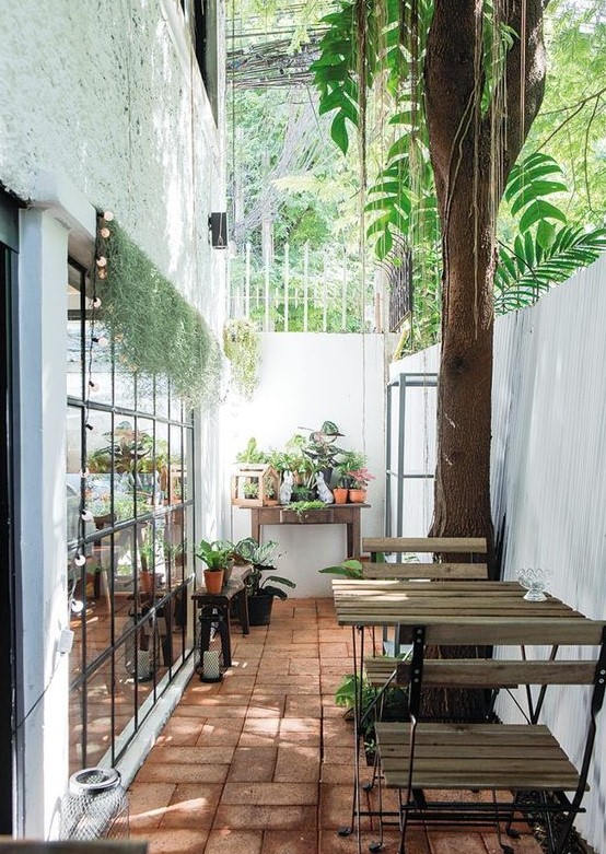a small and narrow terrace with wood and metal folding furnitur,e potted plants and blooms is a lovely space to have a meal or a drink