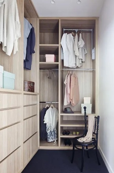 a small and narrow walk-in closet with light-stained drawers, open storage compartments and railings, a black vintage chair