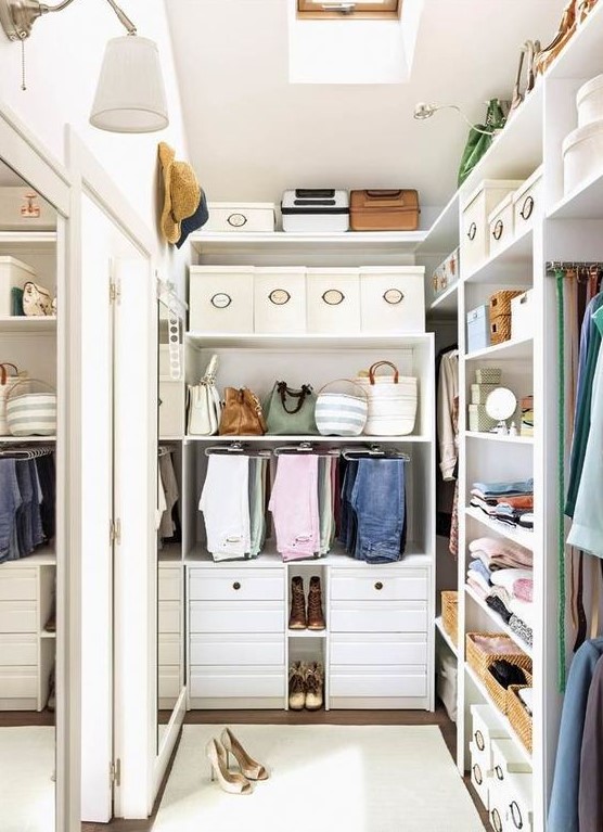 a small and stylish white closet with built-in shelves and drawers, boxes for shoes and hats and a large mirror on the wall