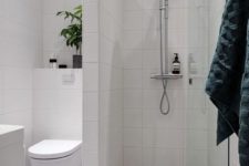 a small bathroom with a shower separate with white long tiles, a printed tile floor, a potted plant and a white vanity