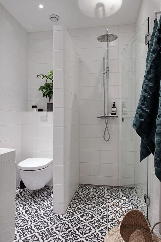 a small bathroom with a shower separate with white long tiles, a printed tile floor, a potted plant and a white vanity