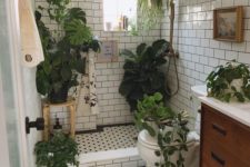 a small boho bathroom clad with white subway tiles, with black and white penny ones, with lots of plants for a forest feel