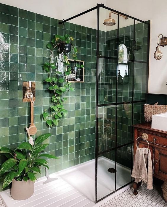 a small bright bathroom with green square tiles, a vintage stained vanity, white appliances and penny tiles on the floor plus potted plants