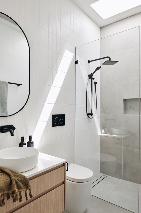 a small contemporary bathroom clad with grey concrete and white skinny tiles, with a stained vanity and black fixtures