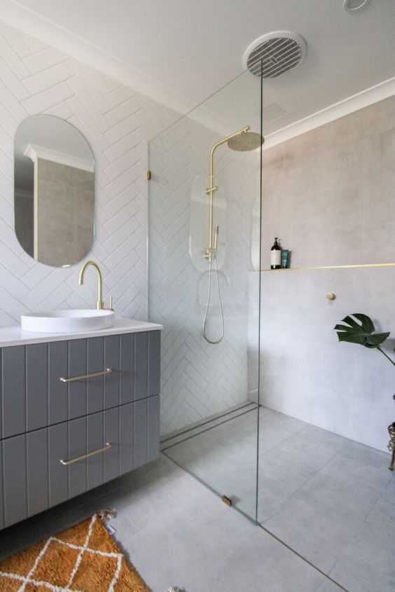 a small contemporary bathroom with grey concrete tiles and white herringbone ones, a grey vanity, gold fixtures is cool