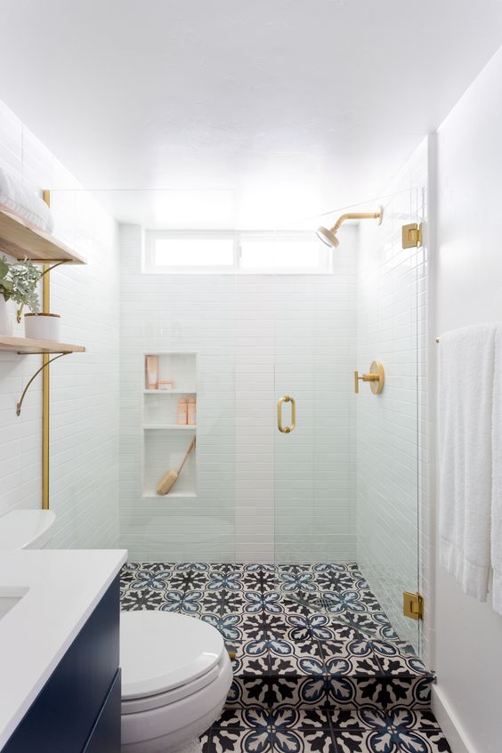 a small contemporary bathroom with white tiles in the shower, patterned tile floor, a navy vanity and touches of gold