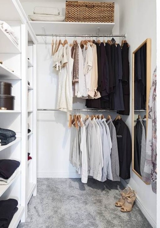 a small contemporary closet with holders for hangers, open shelves for various stuff, a basket and a large mirror