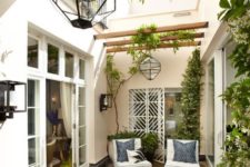 a small contemporary patio in a monochromatic color scheme, with a printed rug, blue pillows, lots of greenery, catchy lanterns and a fire pit