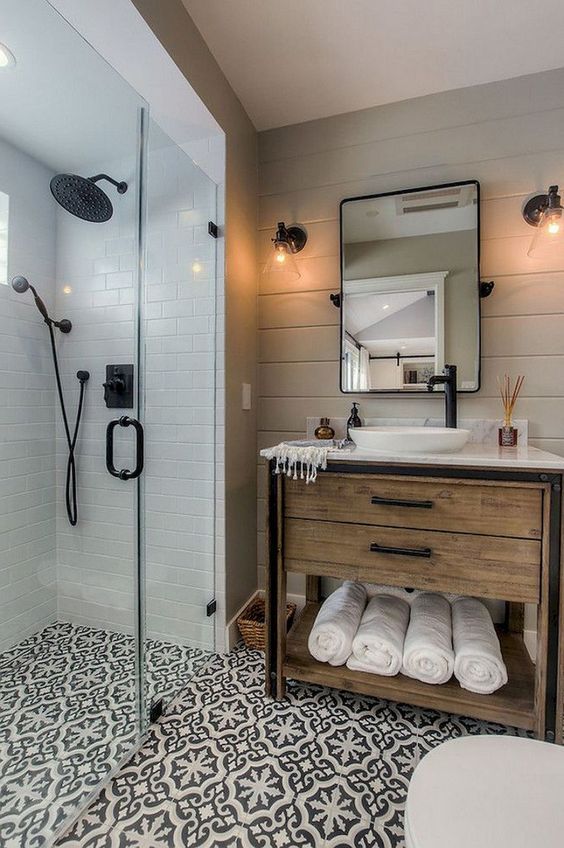 a small farmhouse bathroom with neutral tiles, patterned ones on the floor, a wooden vanity and black fixtures here and there