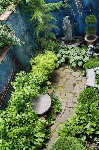 a small garden nook with a vintage statue, some greenery in pots, a bench and lots of greenery around