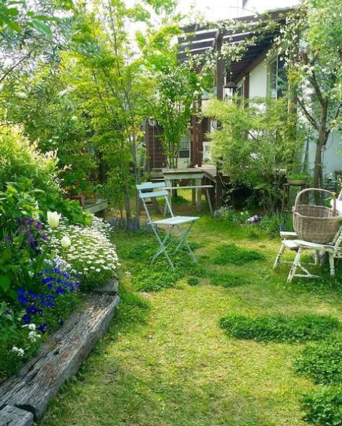 a small garden with a lawn, a flower bed with bright blooms, some vintage garden furniture and some shrubs and trees
