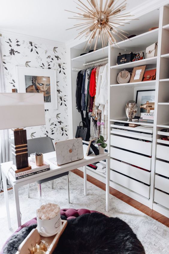 a small glam cloffice with botanical wallpaper, a sunburst chandelier, a simple white desk and an open closet that takes a whole wall