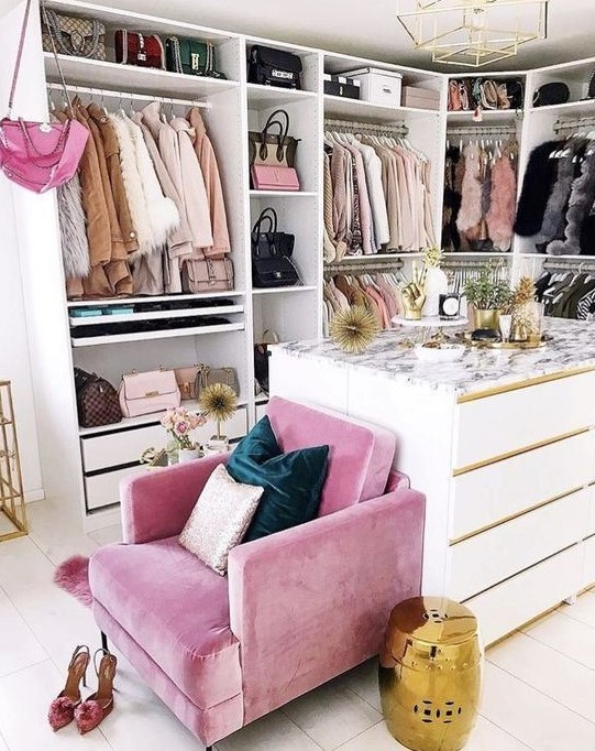 a small glam closet with lots of holders with hangers, shelves and drawers, a large dresser and a pink chair