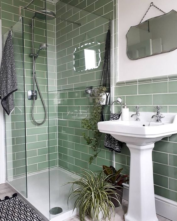 a small green bathroom clad with green subway tiles, with a shower, a free-standing sink and a mirror of a catchy shape