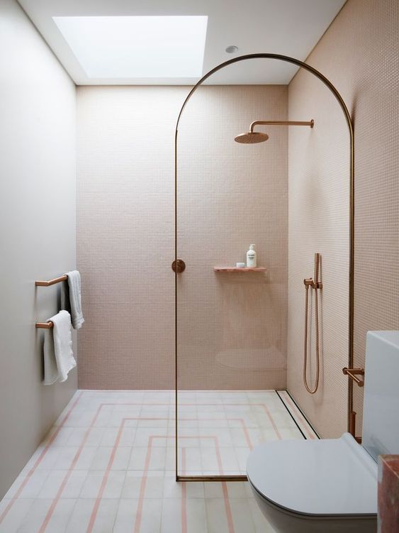 a small minimalist bathroom with pink walls, a printed tile floor, a glass divider and touches of rose gold