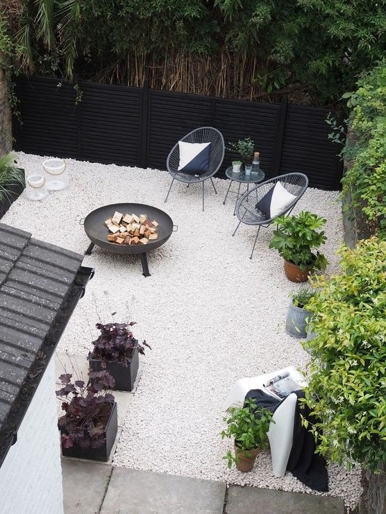 a small modern backyard with white gravel, rattan chairs, a fire pit and some potted plants is super stylish