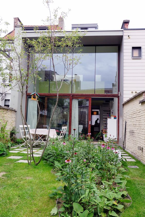 a small modern garden with a lawn, a tree, some blooms and greenery and a white dining set is very simple and cute