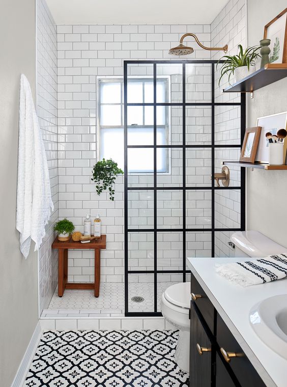 a small monochromatic bathroom clad with printed and white subway tiles, a black vanity, a black framed glass divider and brass touches