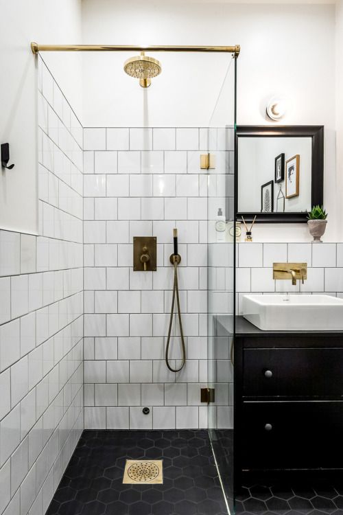 a small monochromatic bathroom with white and black hex tiles, a black vanity and a black frame mirror plus touches of gold