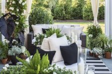 a small monochromatic patio with a striped rug, a black sofa, a bench, candles and lots of greenery and white blooms