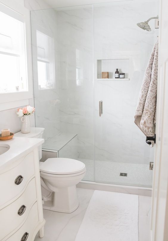 a small neutral bathroom with white marble tiles, a shower space, a white vanity, some neutral textiles is cool