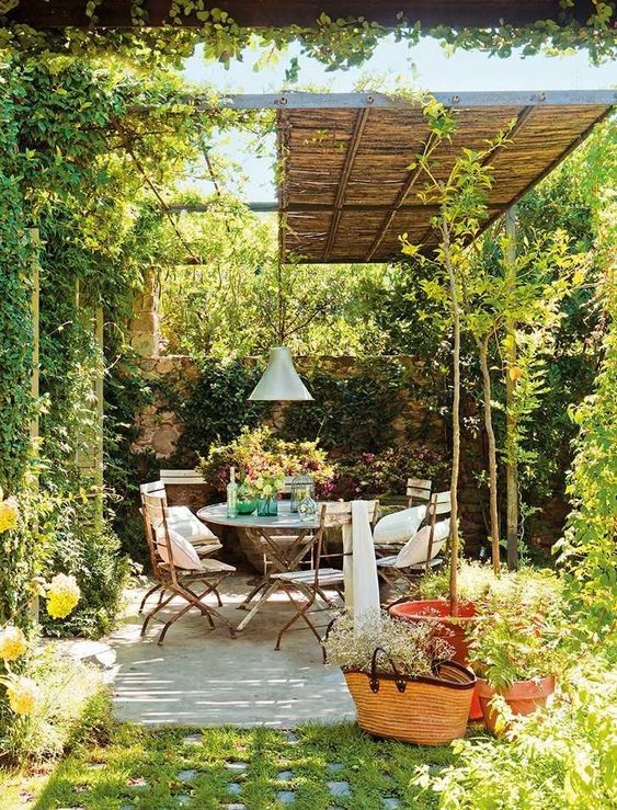 a small patio with a roof, a dining set with folding chairs, greenery and blooms that slowly flows into a garden
