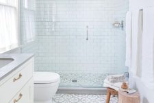 a small serene bathrooms with white subway tiles, patterned ones on the floor, wooden furniture and a window with a curtain