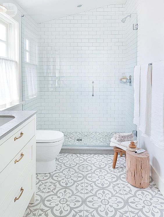 a small serene bathrooms with white subway tiles, patterned ones on the floor, wooden furniture and a window with a curtain